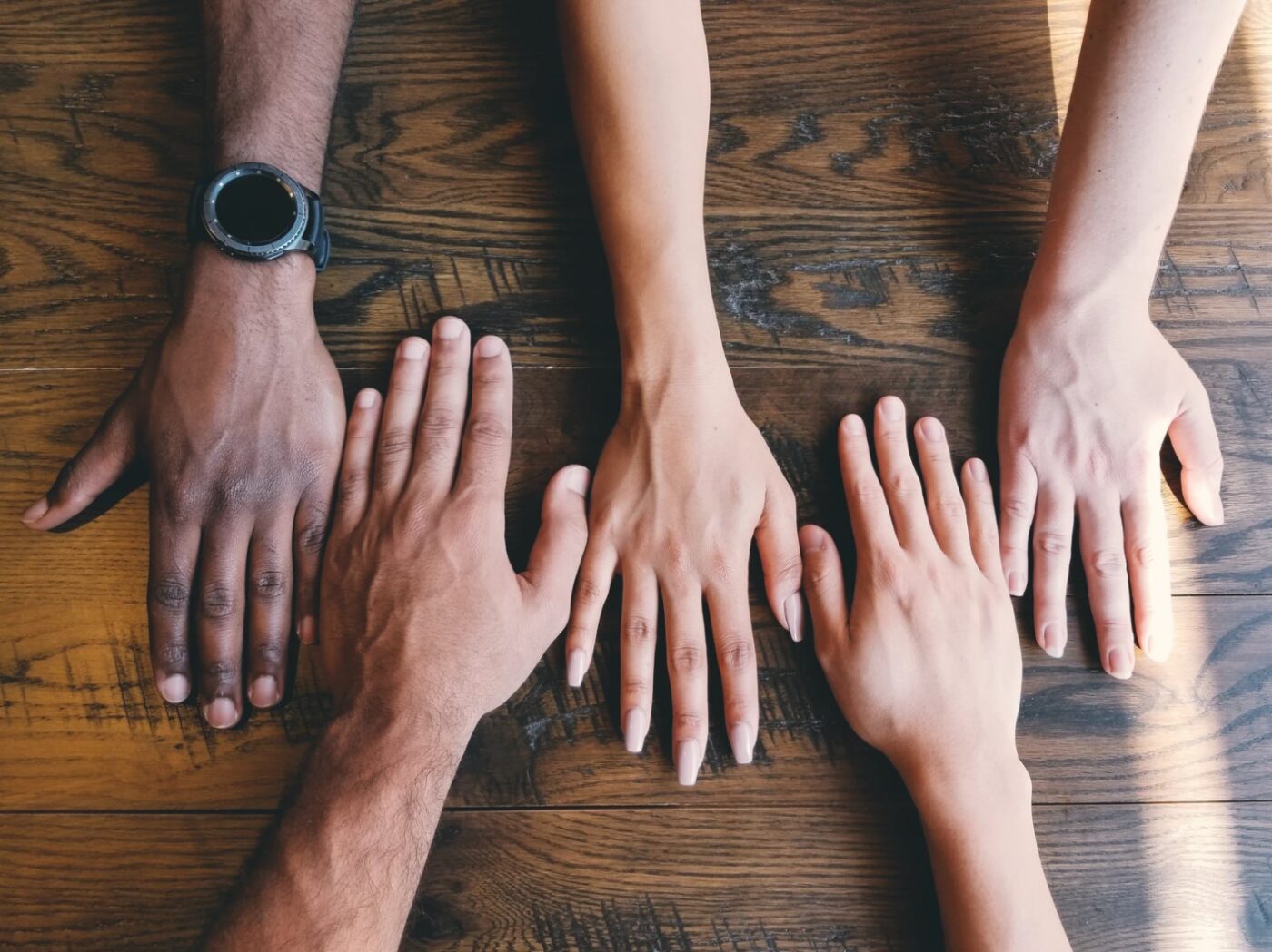 Une main et la base du bras de cinq personnes différentes sont placées côte à côte sur une table en bois fibreux afin de symboliser la diversité et la solidarité.